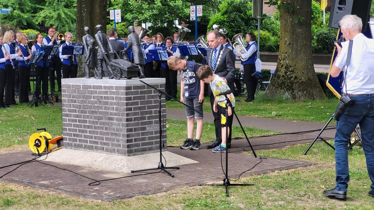 Burgemeester Mark Slinkman, kinderburgemeester Kyan Pas en een Oekraïens kind leggen samen een bloemstuk bij het Evacuatiemonument